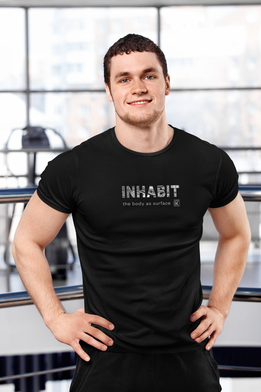 Man wearing a black t-shirt with 'INHABIT' text in a gym setting
