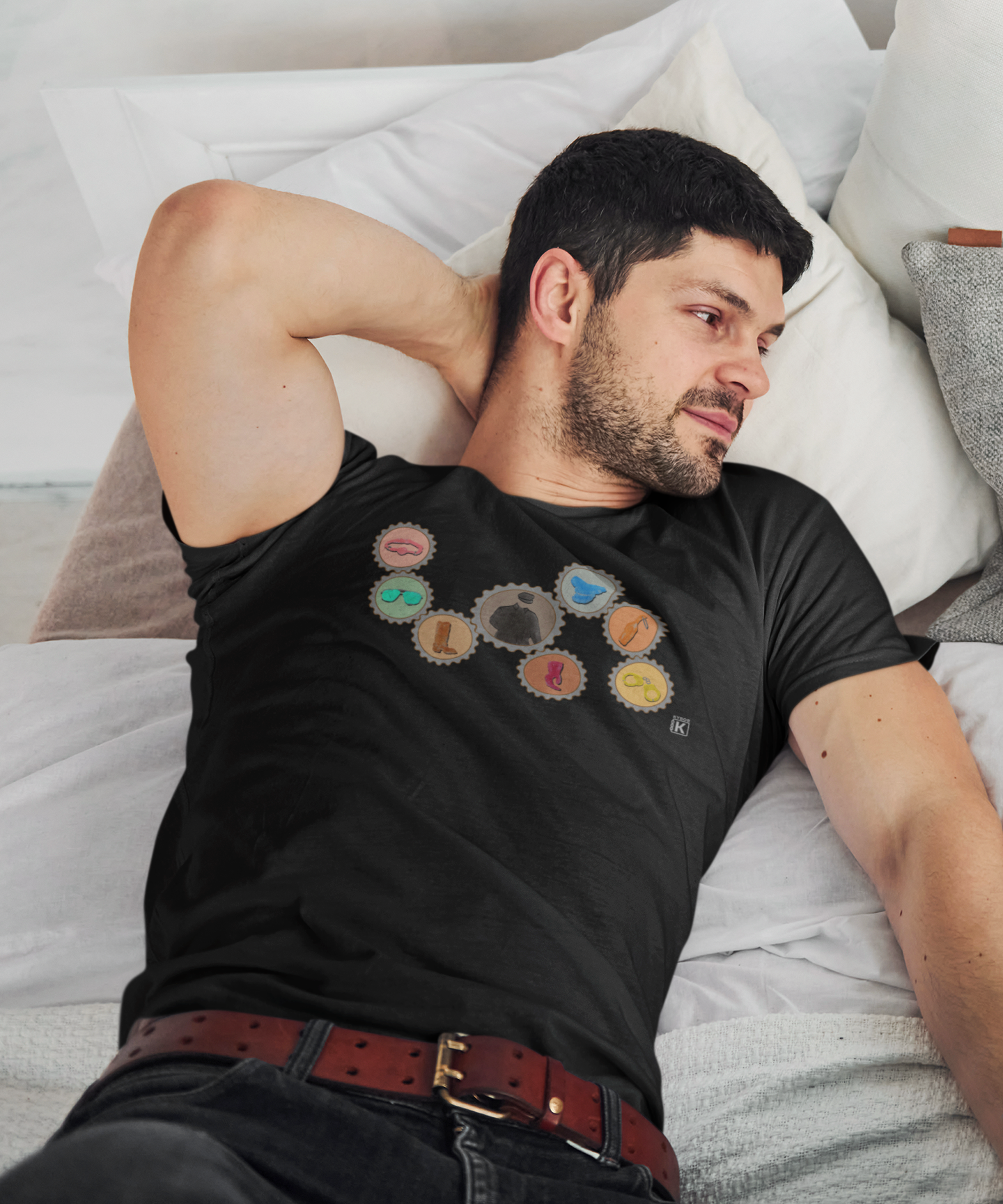 Man wearing a black t-shirt with colorful designs, lying on a bed.