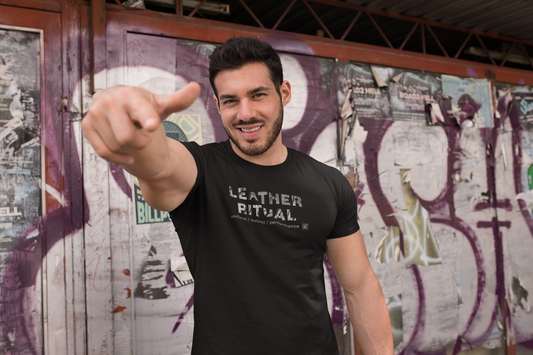 Man wearing a black t-shirt with 'Leather Ritual' text, pointing forward against a graffiti-covered wall.